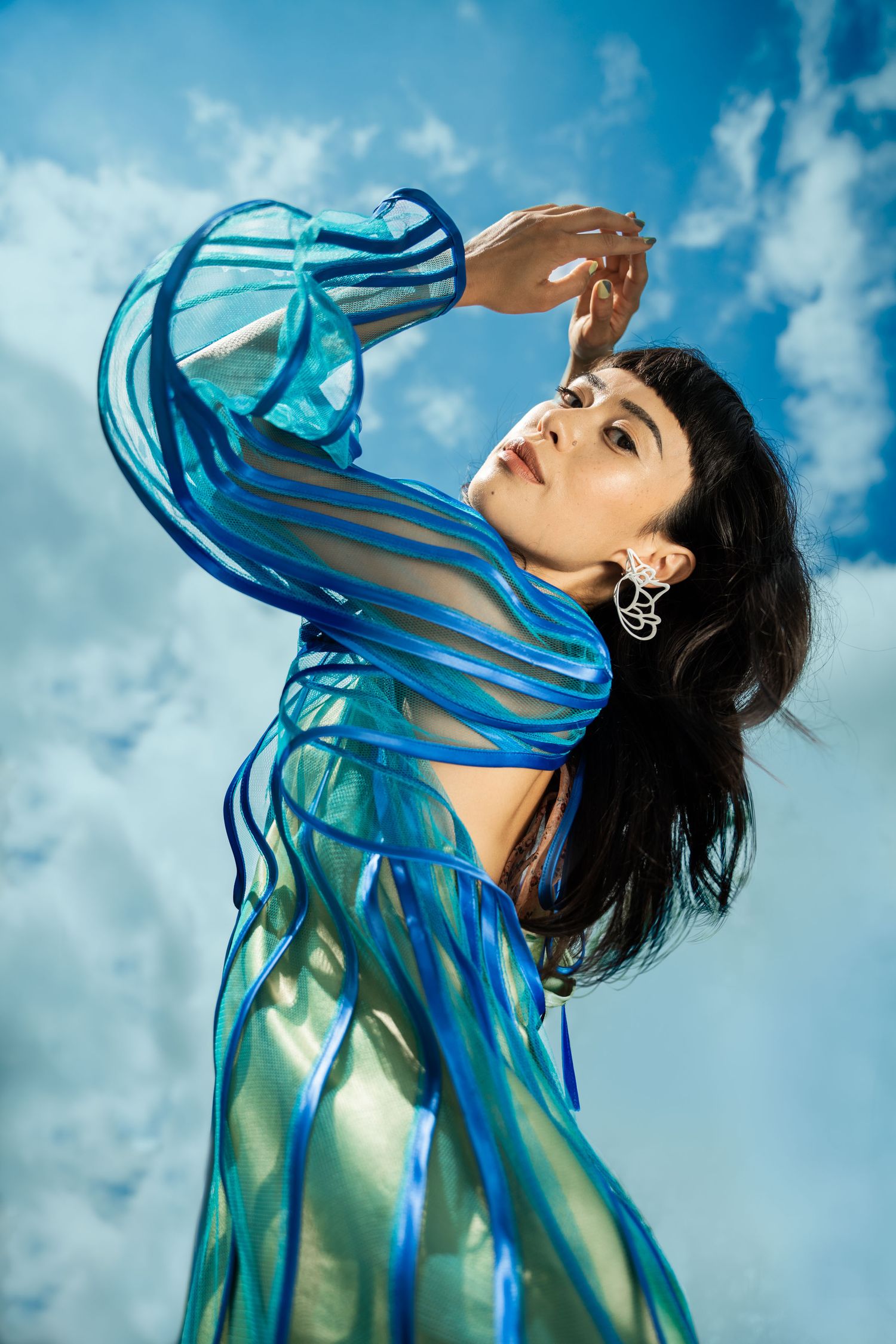 A woman in a blue patterned dress lying in shallow water with reflections; fine art fashion and creative editorial photography.
