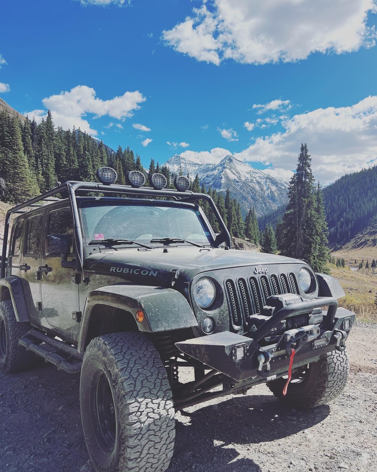 Row of modified Jeep Wranglers parked in mountainous terrain with snow-capped peaks.