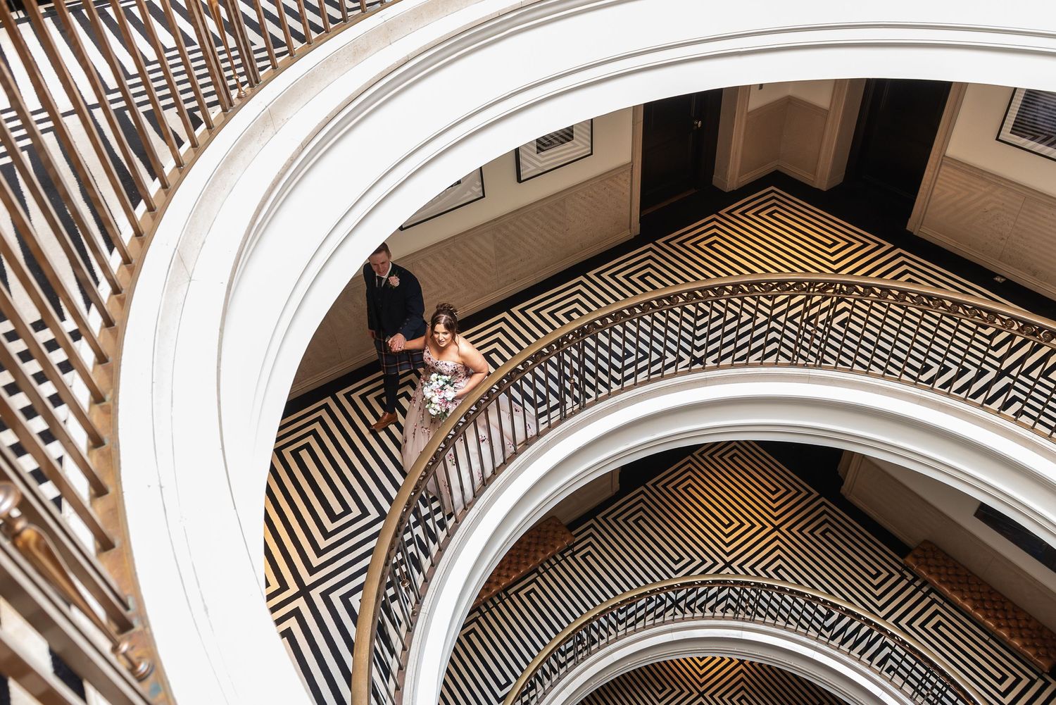Bird's eye view of couple standing on geometric patterned floor under curved white architecture. The Edinburgh Grand makes a great wedding
