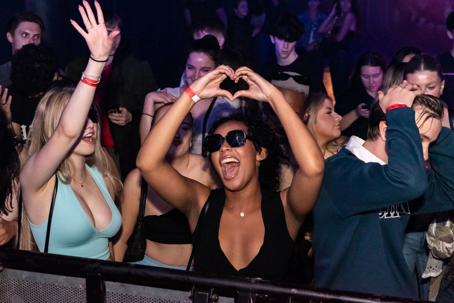Energetic crowd dancing and having fun at a dark nightclub with hands raised in the air.
