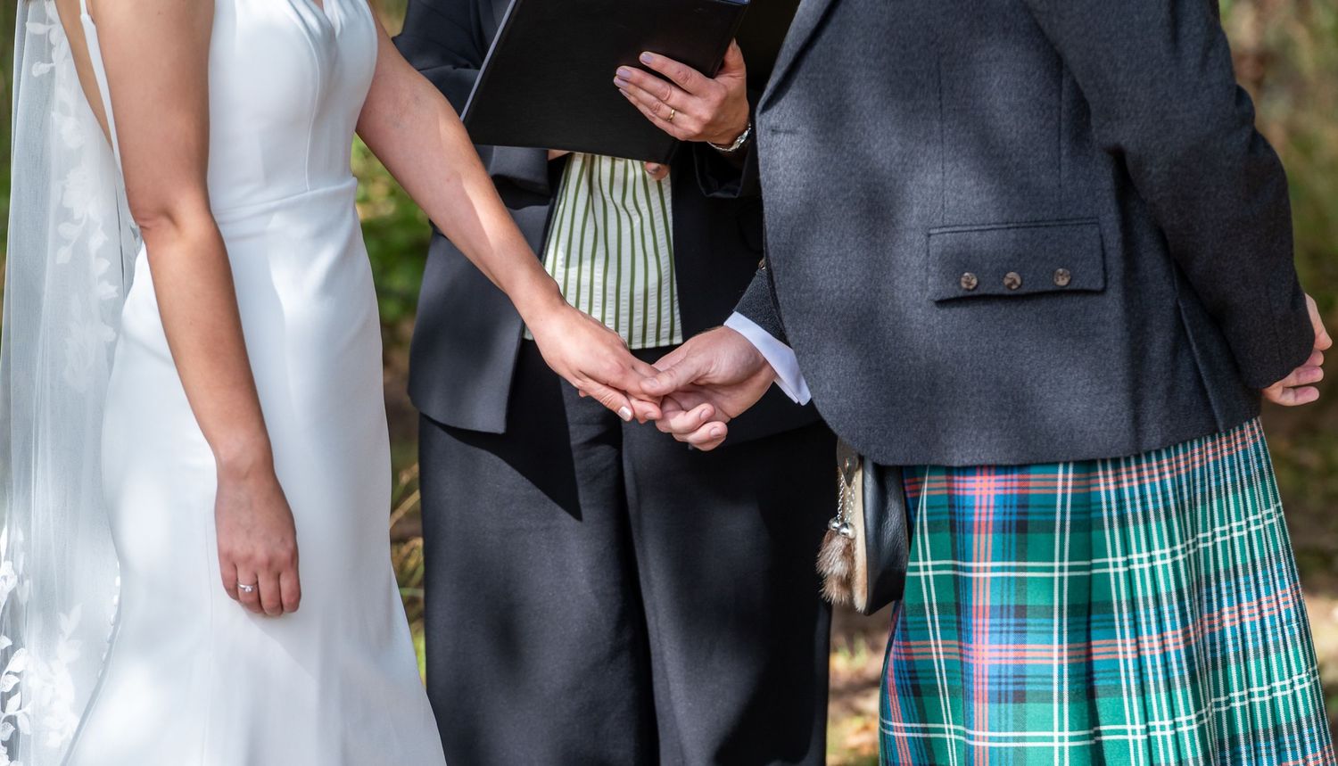 A group in formal attire stands together at an outdoor event, with men wearing kilts and suits.