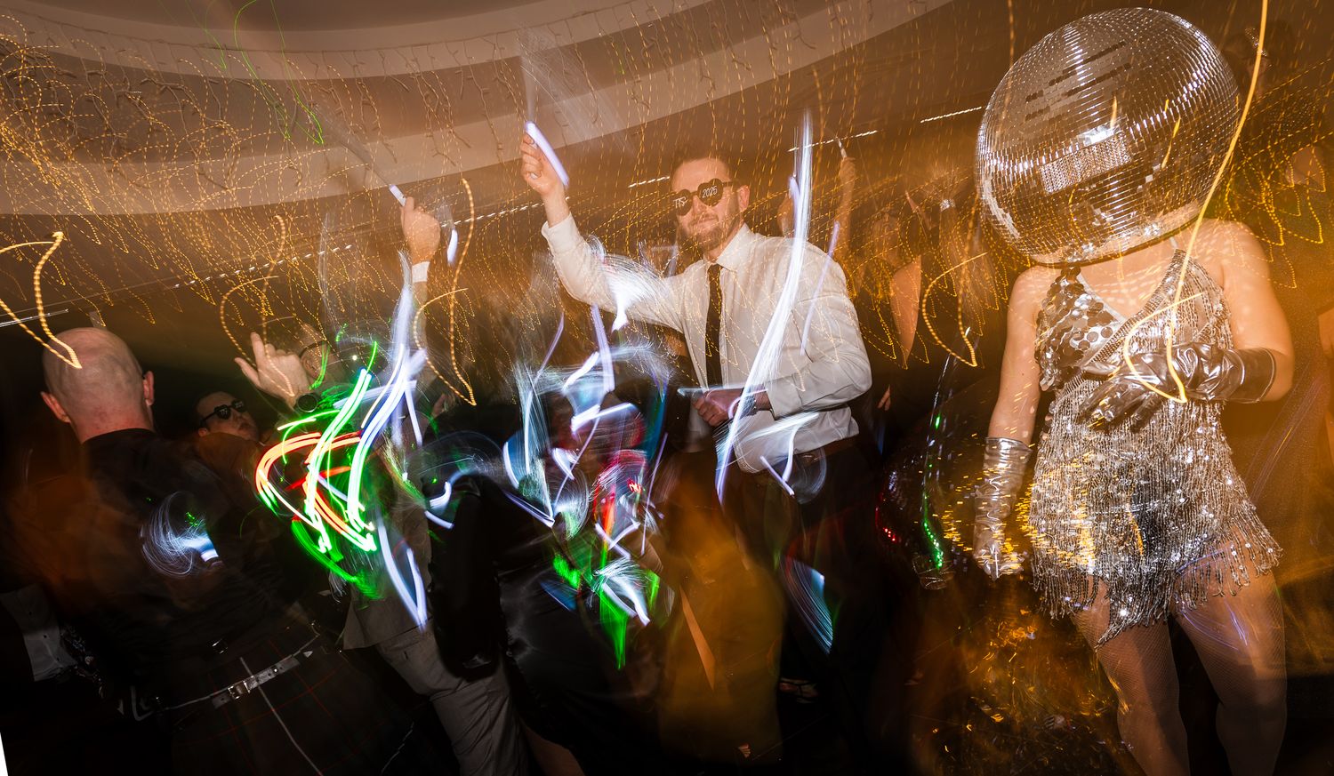 Party guests dancing at a wedding reception with light trails and motion blur creating a dynamic nightclub atmosphere.