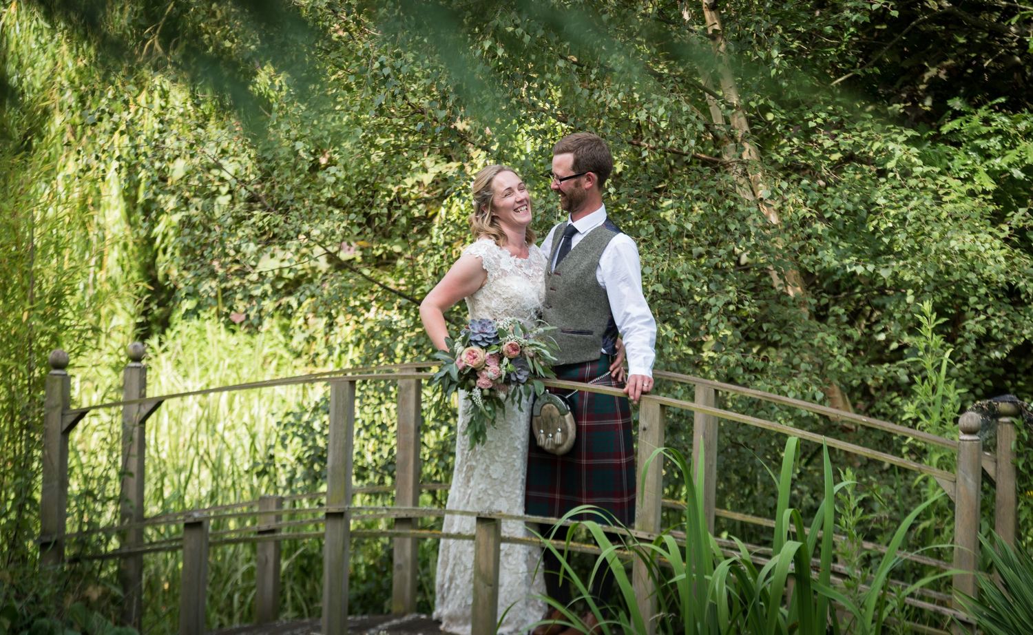 A couple embraces during an outdoor summer wedding ceremony surrounded by lush greenery and natural light in Dunbar, East Lothian.