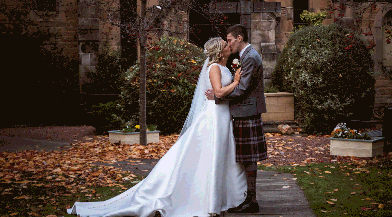 A romantic wedding couple shares intimate moments in a beautiful garden setting with stone walls and autumn foliage.