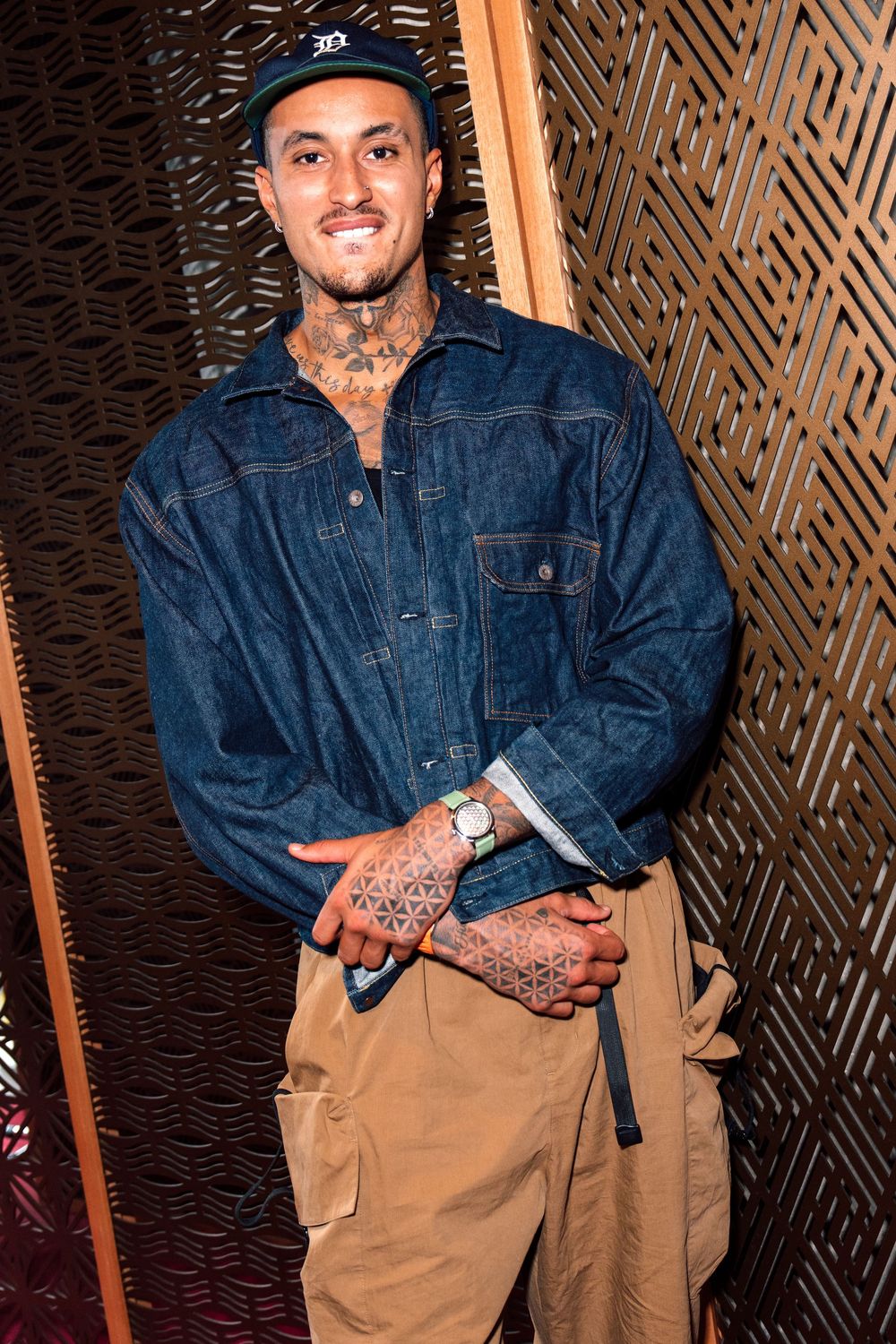 Kyle Kuzma in Detroit Tigers cap and denim jacket with khaki cargo pants poses against patterned wall in Zuma Hong Kong