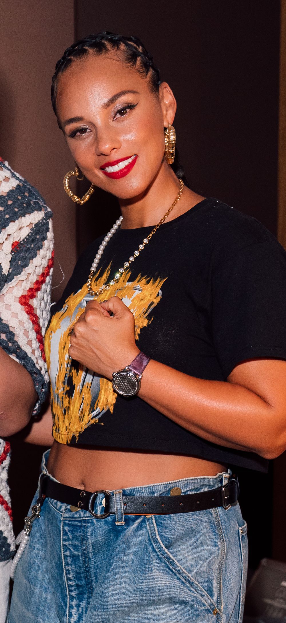 Alicia Keys wearing black crop top and jeans posing with the Watch Ho and Co Selten watch and dramatic red lipstick against dark background.