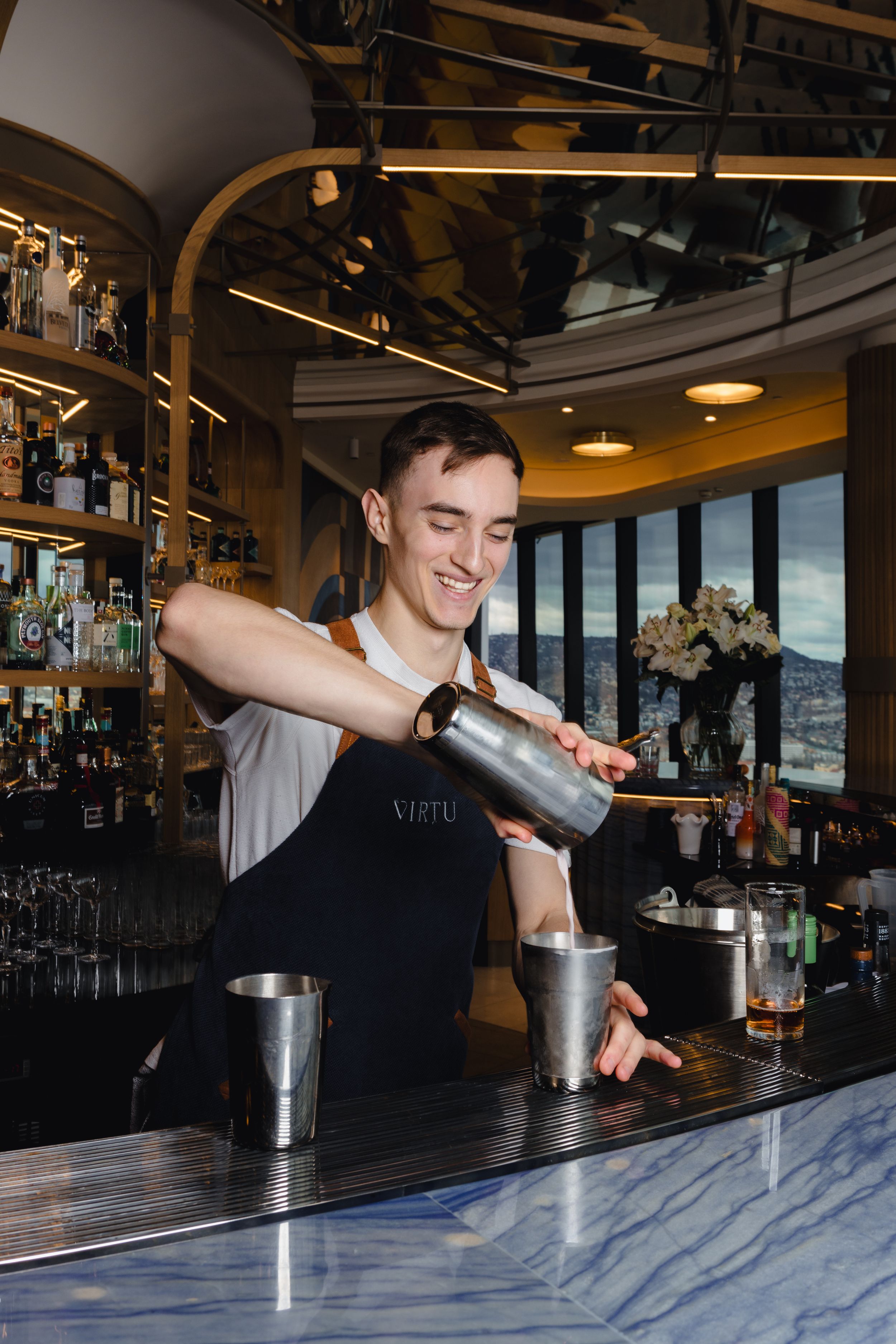 Bartender pouring and mixing drinks at an upscale bar with modern marble countertop.