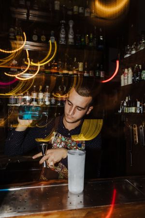 Bartender crafting cocktail with colorful light trails in dark bar atmosphere.