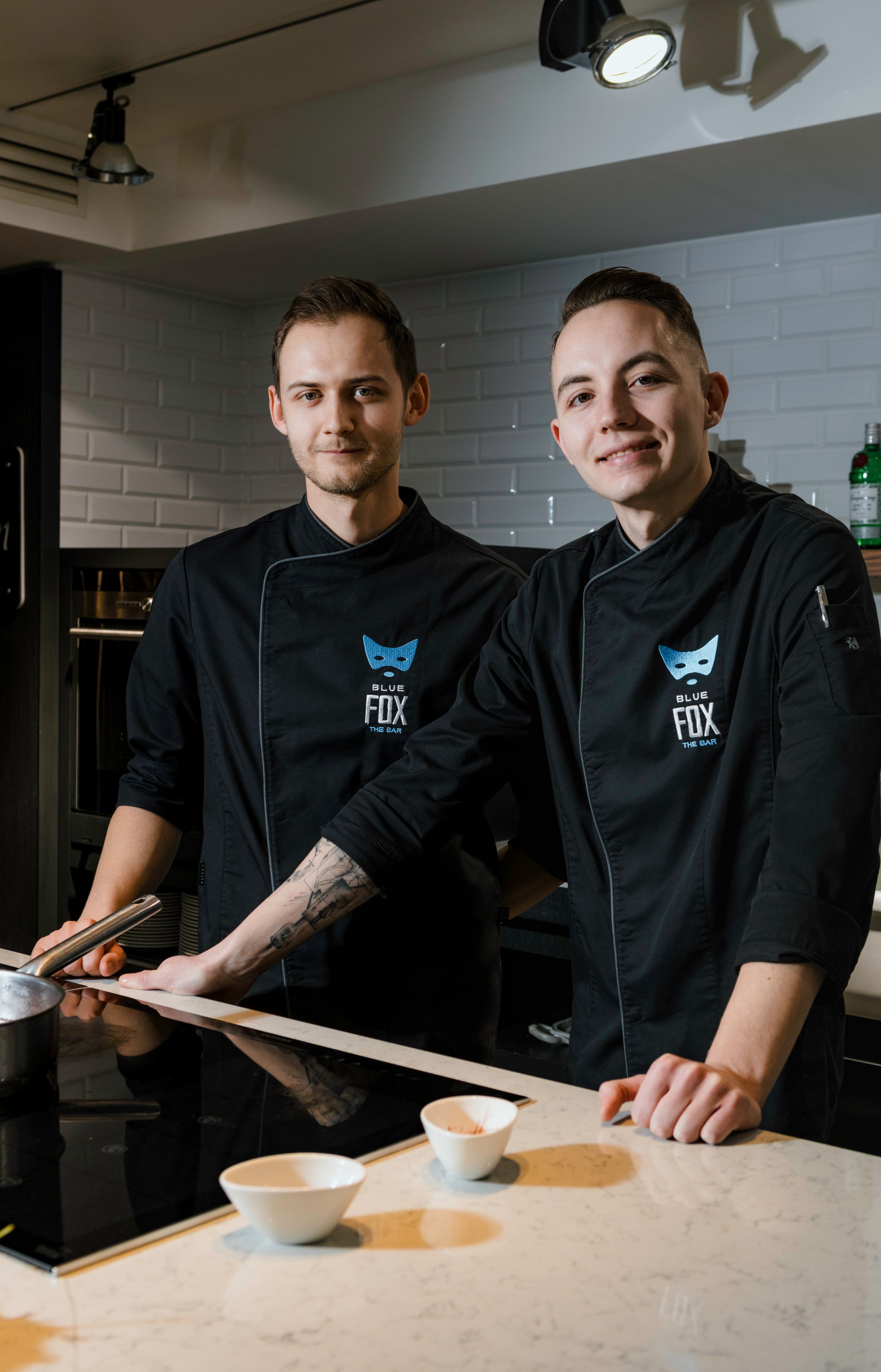 Two chefs in black uniforms with blue fox logos preparing ingredients at a counter.