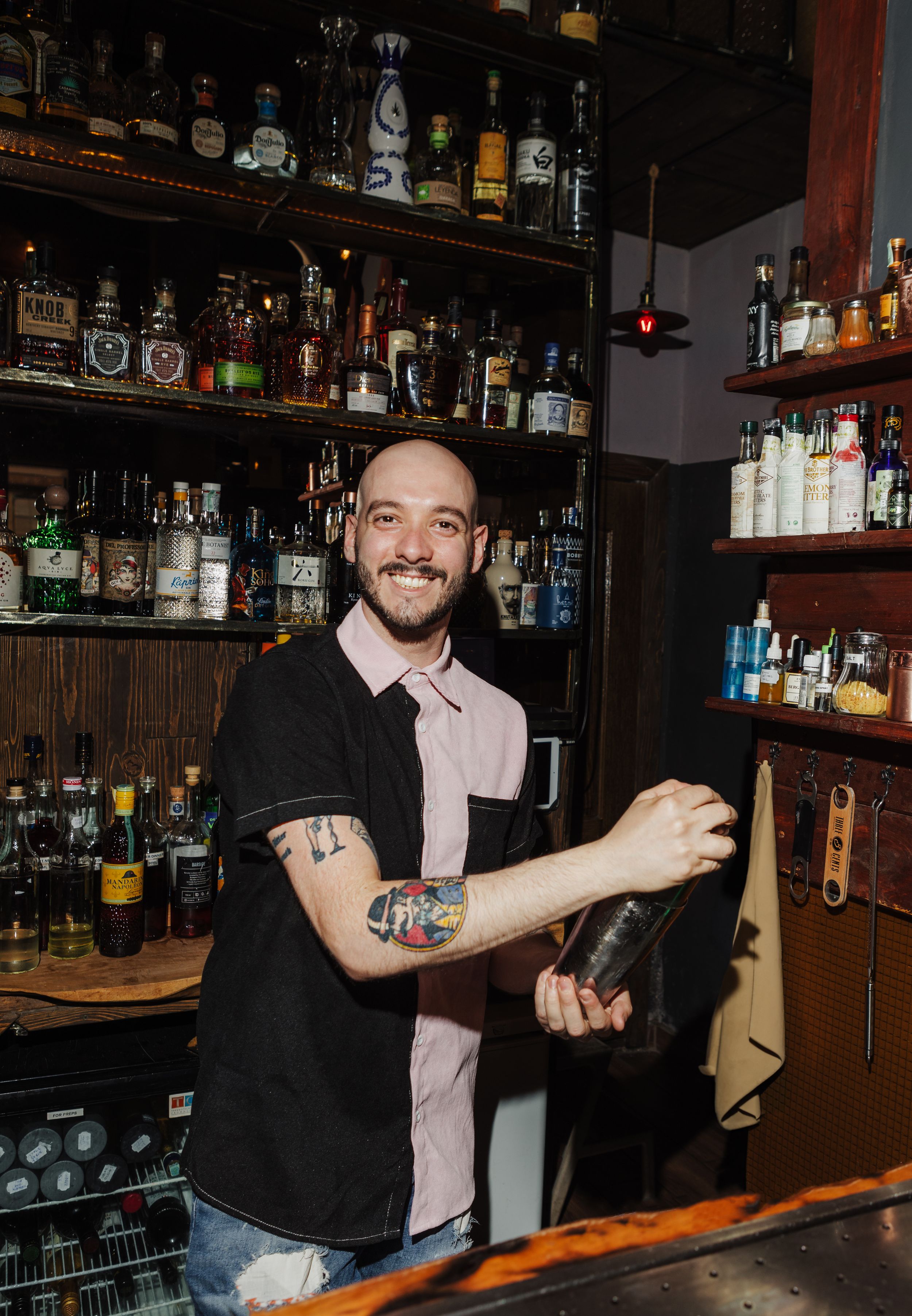 Bartender mixing drinks behind well-stocked bar with various liquor bottles on display.
