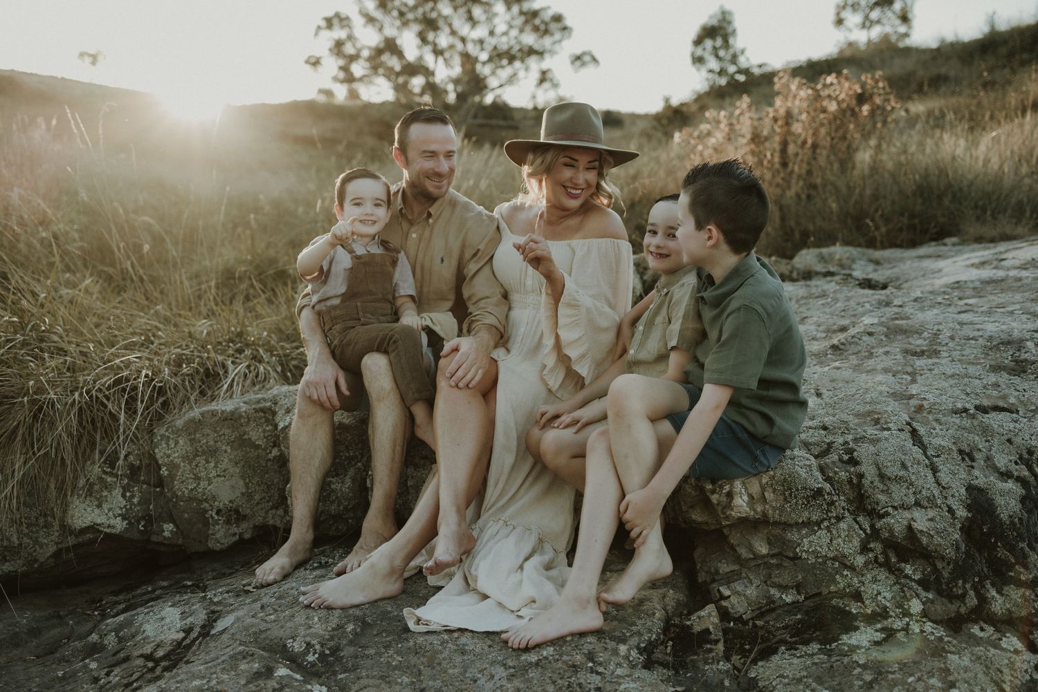 A happy family sits together on Googong rocks at sunset, creating a warm and intimate outdoor scene in golden light.