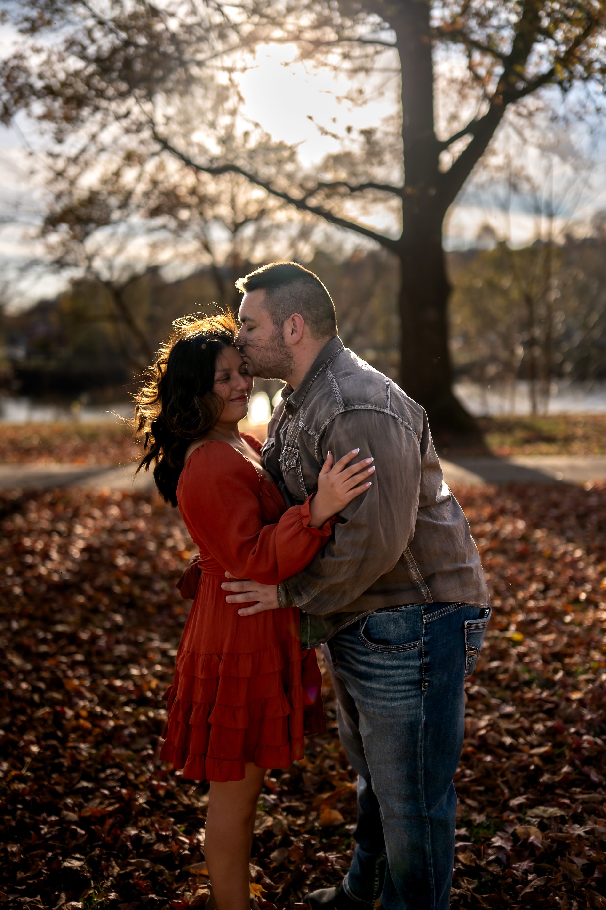A couple embraces in a romantic moment surrounded by fallen autumn leaves at sunset.