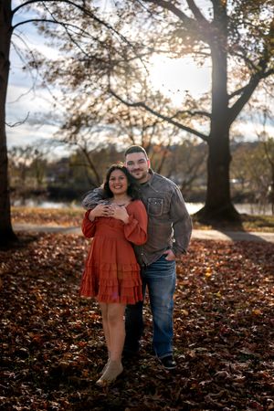 A couple shares joyful moments together while posing on fallen autumn leaves during a sunset photo session.
