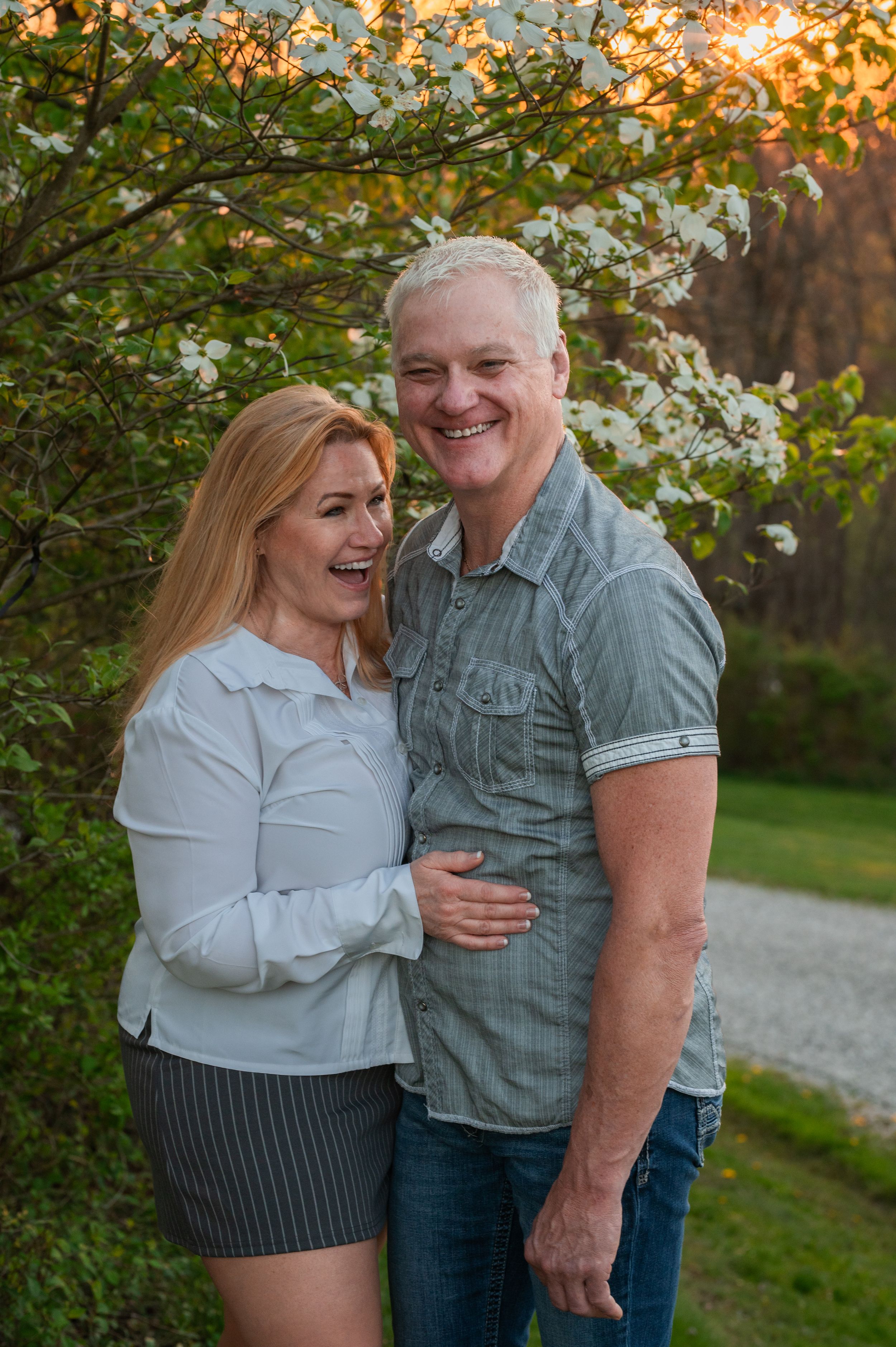 Happy couple laughing together under flowering trees during sunset.