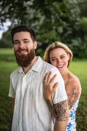 A couple shares a playful moment outdoors, wearing summer clothing with the person in white having visible tattoos.