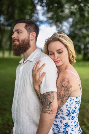 A couple embraces intimately in a garden setting with one wearing a white shirt and one in a blue floral sundress.