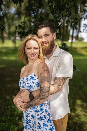 A tender embrace between a couple in a green outdoor setting wearing white and blue floral clothing.