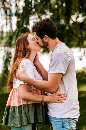Romantic couple sharing an intimate kiss outdoors in a natural setting with sunlit trees in the background.