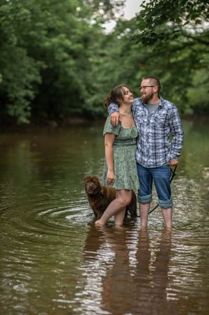 Couple standing in creek water with their brown dog enjoying a romantic outdoor moment.