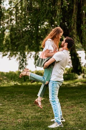 Playful couple sharing a romantic moment as he lifts her up in a park setting.