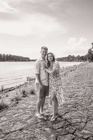 A romantic black and white photo of a couple embracing on a rocky shoreline beside a lake.