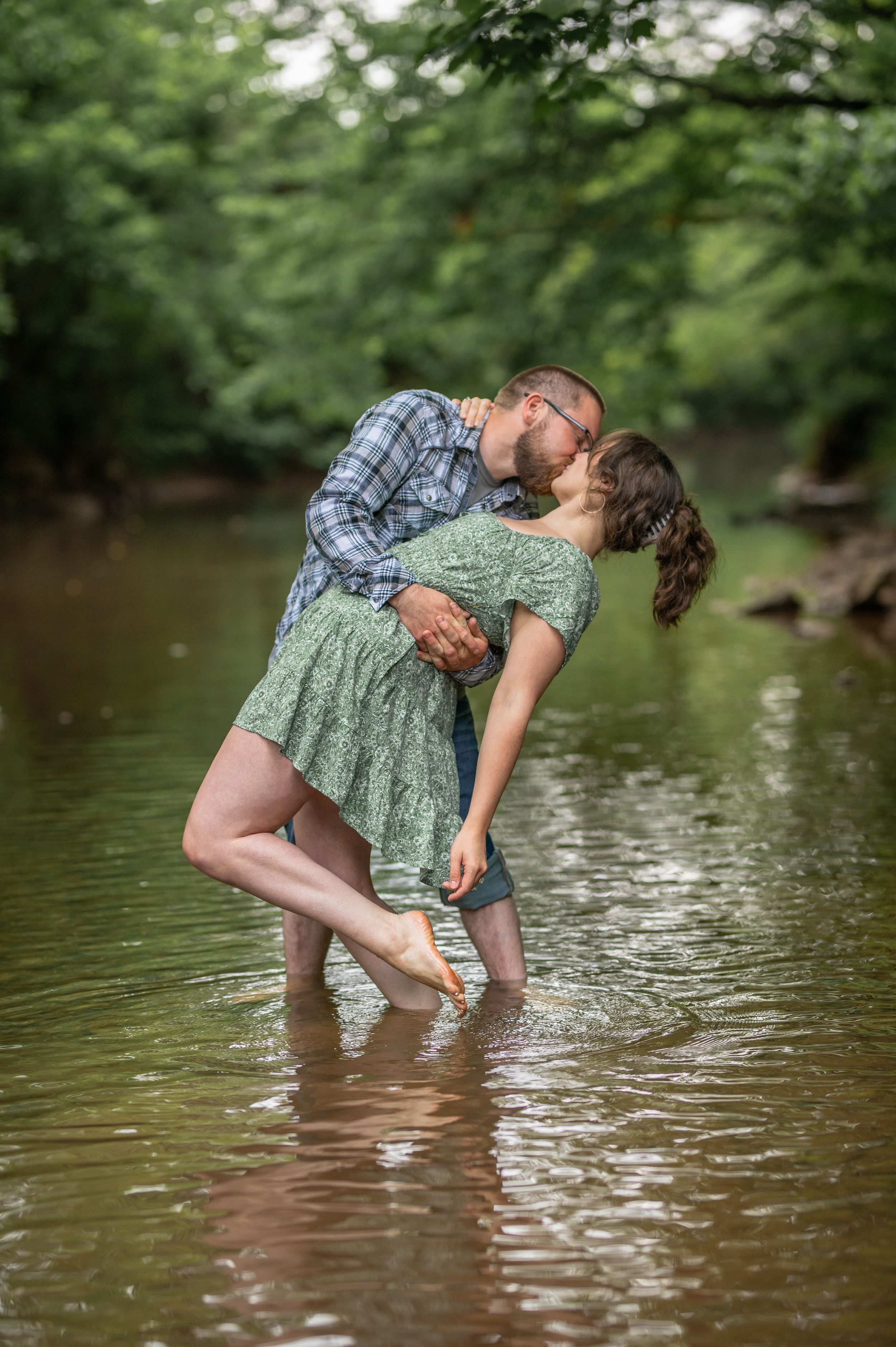 Romantic couple embracing while standing in a creek surrounded by lush greenery.
