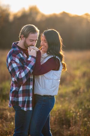 A romantic couple embraces during sunset in a field of tall grass and wildflowers.
