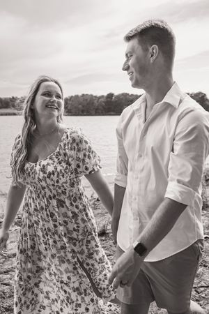 A couple laughs and enjoys moments together by the water in black and white photos.