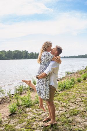 Two people share a romantic embrace on a scenic riverbank during a sunny summer day.