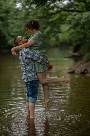 Playful couple embracing in creek water during romantic photoshoot.