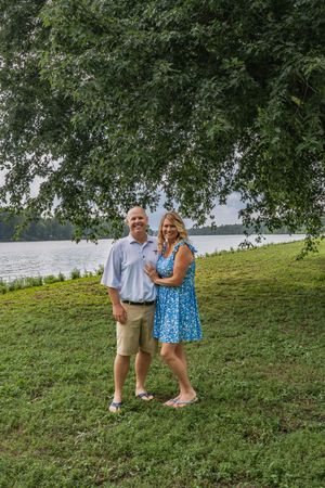 A happy couple poses together on a grassy hillside with a lake visible in the background.