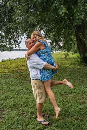 A playful couple shares a fun moment on a grassy hill with trees in the background.