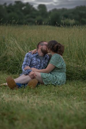 Romantic couple sharing an intimate moment while sitting in a tall grass meadow at dusk.