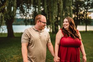 A couple in burgundy and tan casual wear share intimate moments while walking in a scenic park during golden hour.