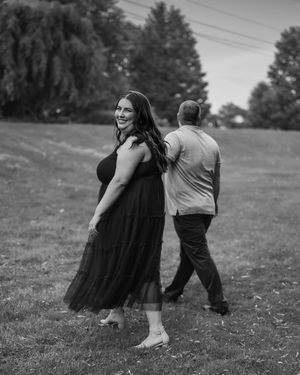 Two people playfully spin and dance together in a grassy field with a dark silhouetted tree line in the background.