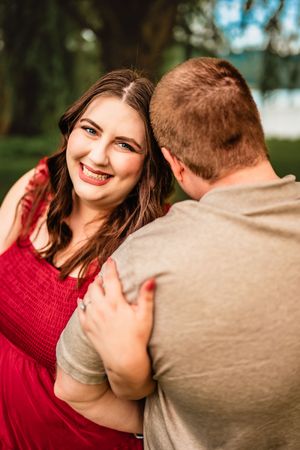 A couple in casual attire share a playful, romantic moment outdoors with expressions of joy and laughter.