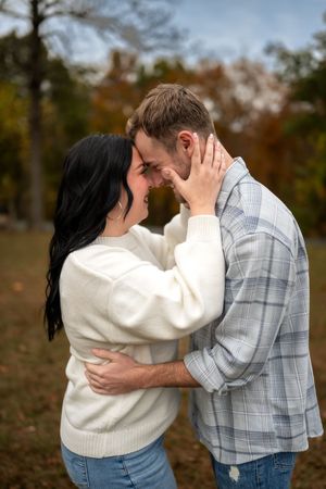 A couple in casual fall attire share tender moments in a romantic outdoor photoshoot series with autumn trees in background.