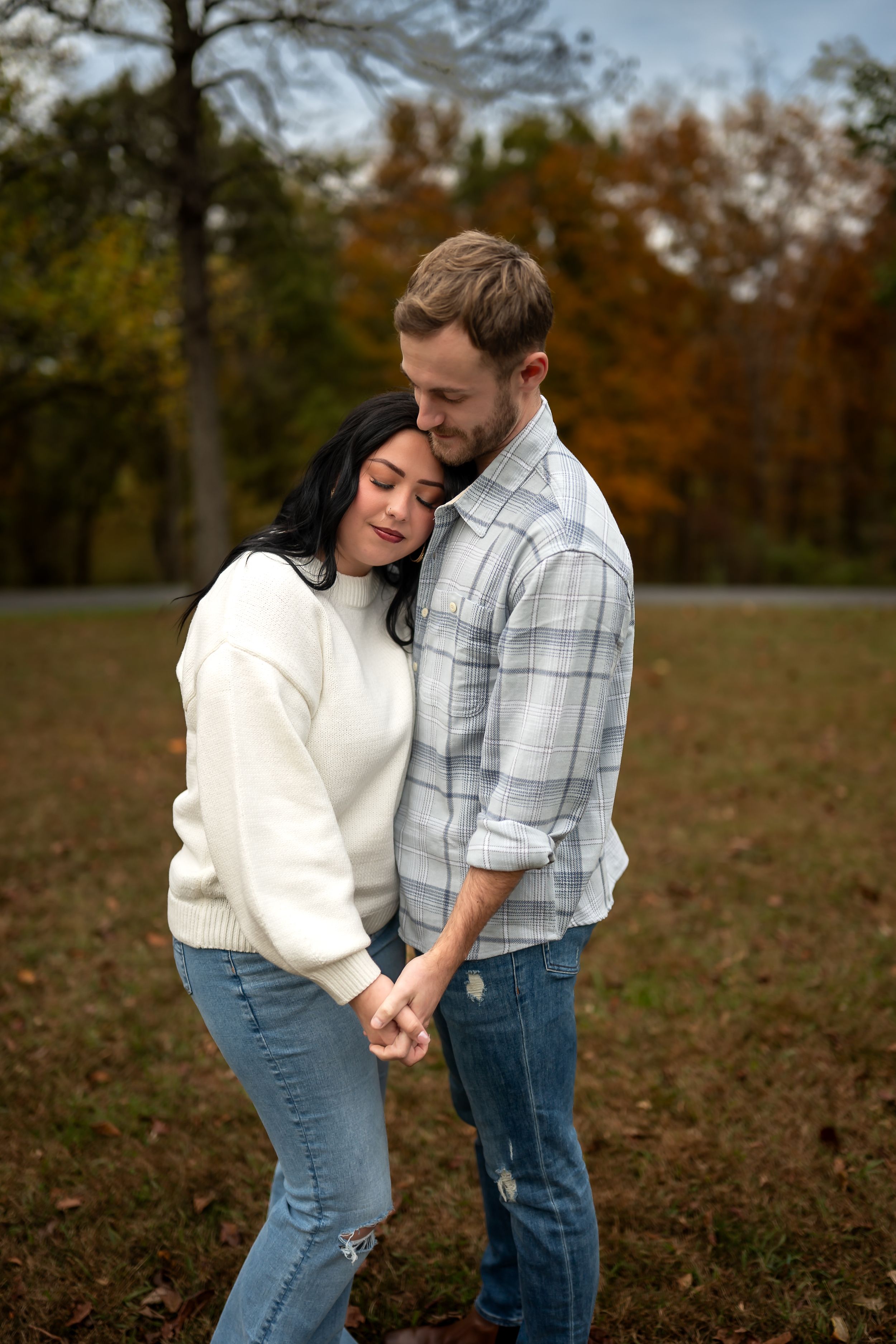 A tender moment between a couple in casual wear, dancing together in a field during fall season.