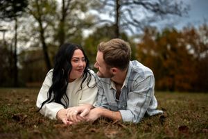 A couple lies in fallen autumn leaves while sharing a tender moment outdoors during fall season.