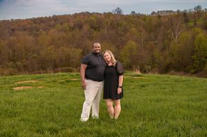 Couple standing together in casual attire on a grassy hillside landscape.