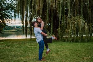 Romantic couple embraces in a lush green park setting during an outdoor engagement photo session.