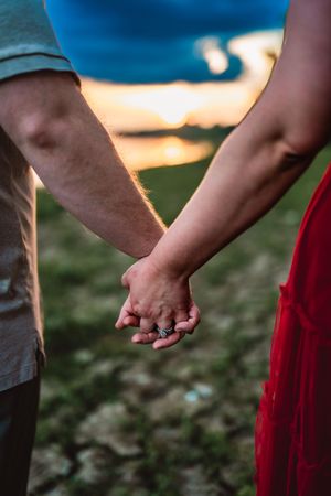 Two people holding hands and gradually releasing their grip during sunset in a romantic outdoor setting.