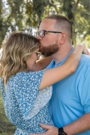 Couple sharing tender embrace in sunlit garden setting.