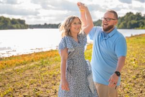 Couple dancing playfully by riverside during autumn afternoon.