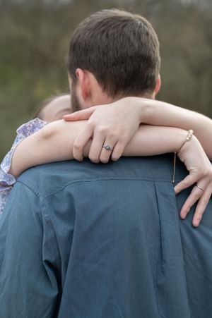 Close-up of hands with engagement ring embracing from behind.