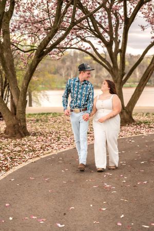 Couple walking hand in hand on path beneath spring cherry blossoms.