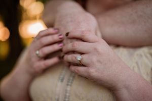 An engagement ring sparkles as hands are clasped together in a romantic moment.