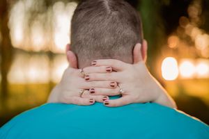 Two hands with red nail polish touch and hold each other in a romantic moment at sunset.