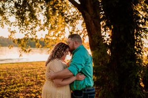 Two people share an intimate embrace under a sunset-lit tree during a romantic autumn photo session.