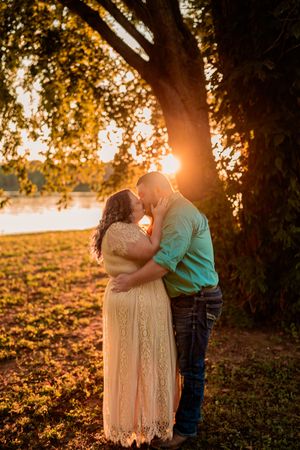 A romantic couple embraces beneath a tree at sunset, with golden sunlight filtering through autumn leaves.